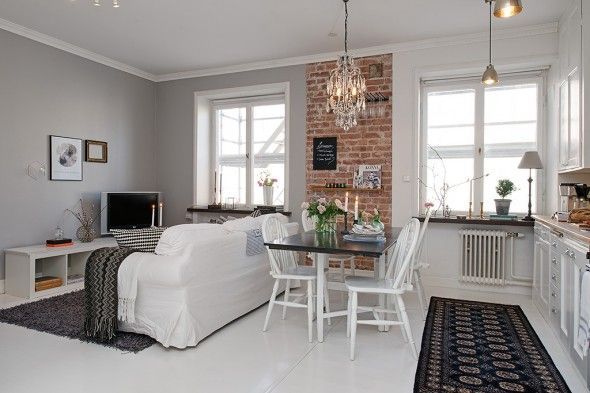 a living room and dining area with brick wall, white furniture and black rugs