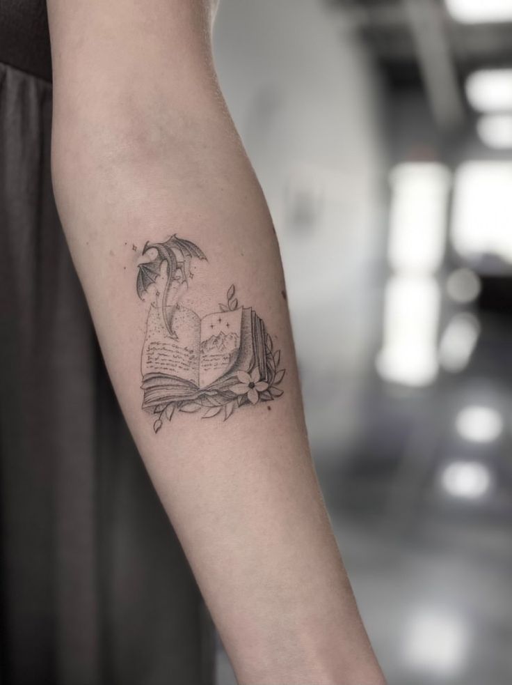 a woman's arm with a book and an umbrella tattoo on her left forearm