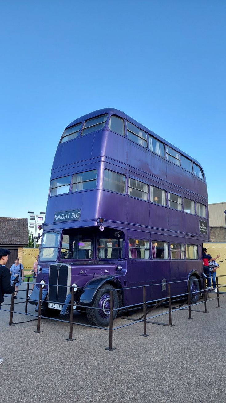 a purple double decker bus parked in front of a building with people standing around it