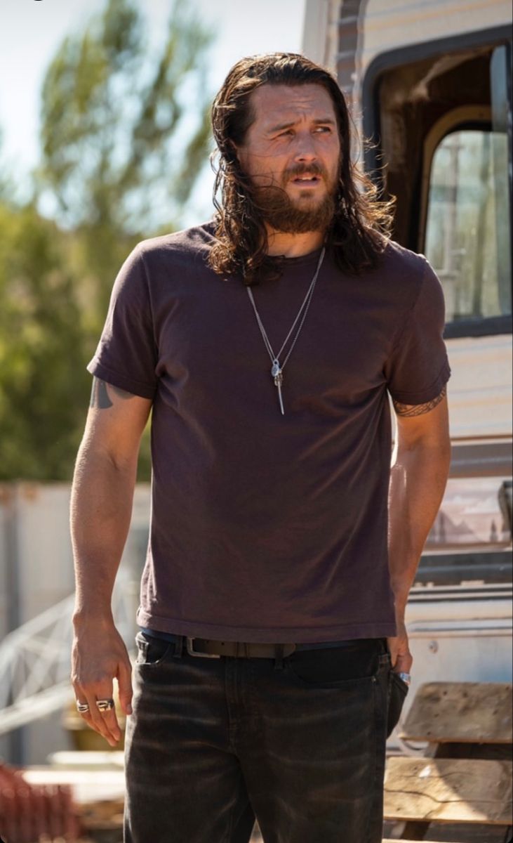 a man with long hair standing in front of a truck