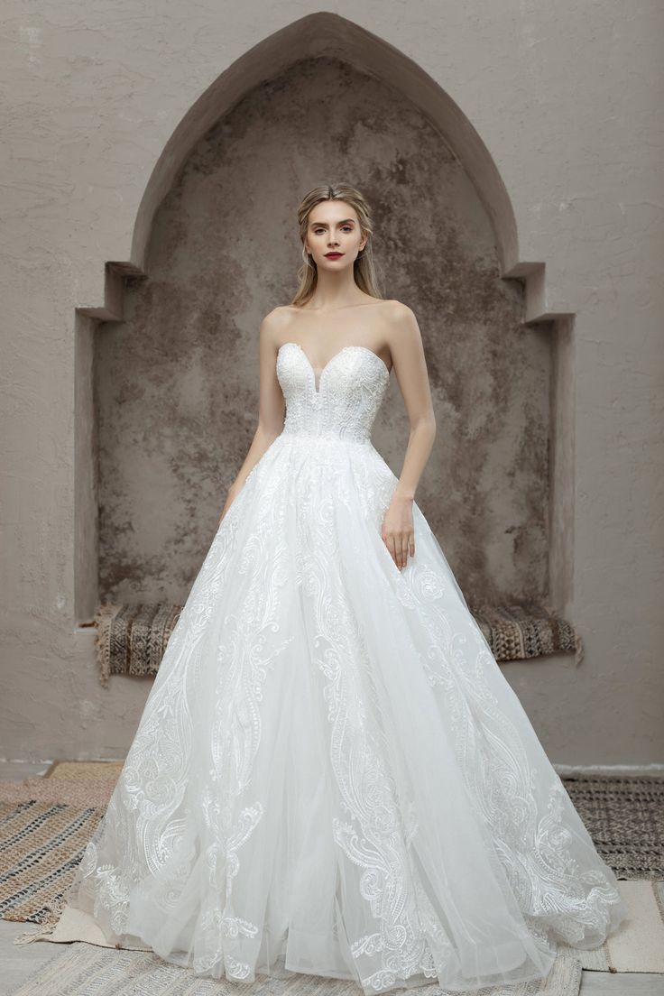 a woman in a white wedding dress standing on a rug with an archway behind her