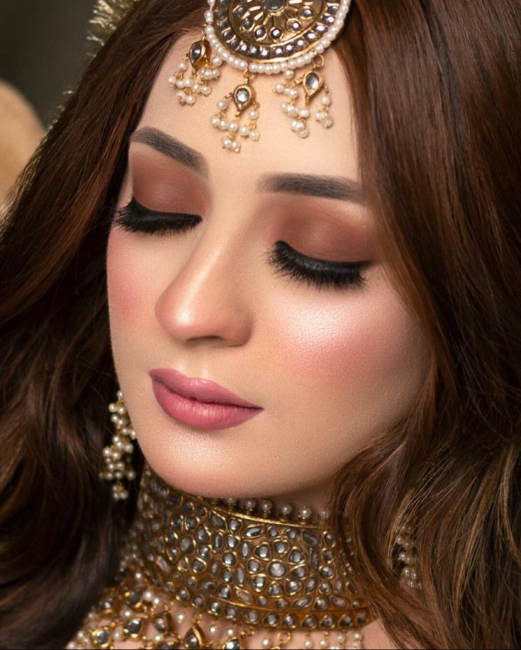 a woman with dark hair wearing a gold headpiece and jewelry on her face, looking down