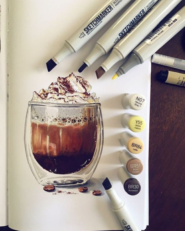 an open book with markers and pens on it next to a cup filled with liquid