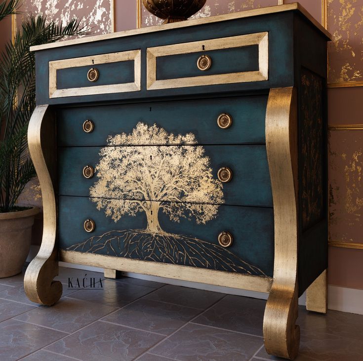 a blue and gold dresser with a tree painted on the front, sitting next to a potted plant