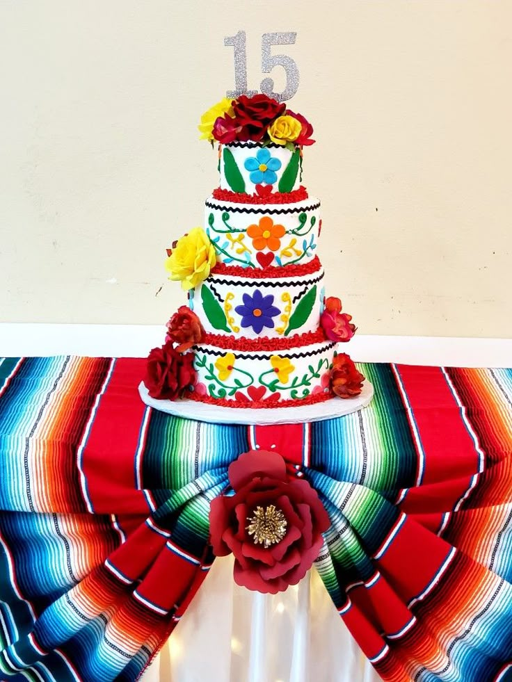 a multi - tiered cake is decorated with flowers and ribbons on a colorful table cloth