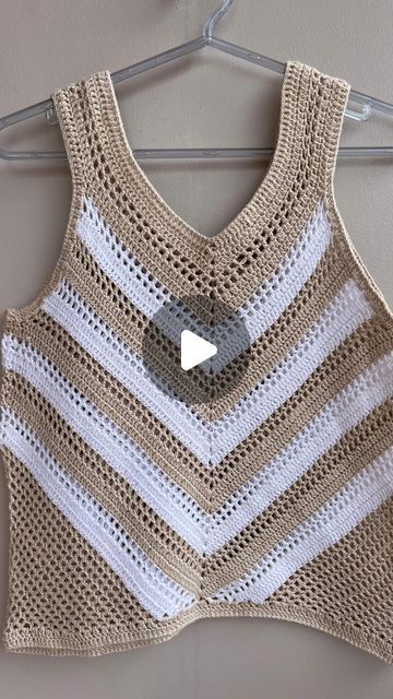 a crocheted top hanging on a hanger with a video button in the middle