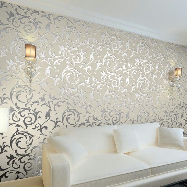 a white couch sitting in front of a wall covered in silver and white damask