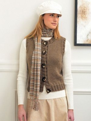 a woman standing in front of a wall wearing a hat and scarf with buttons on it