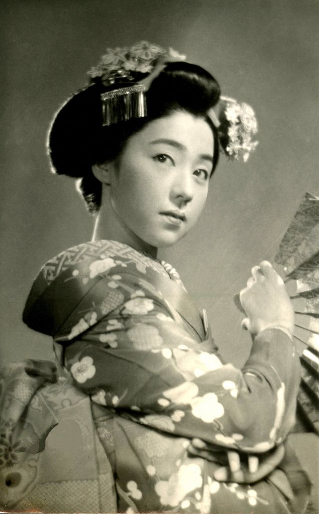 an old photo of a woman in kimonos holding two fan's and looking at the camera