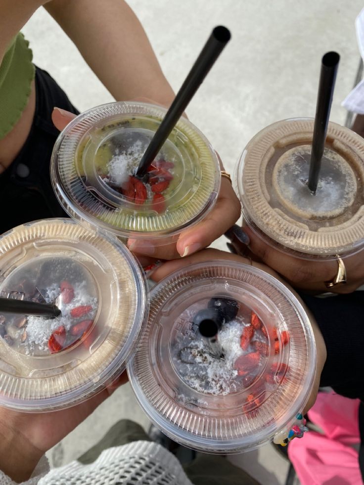 three people holding plastic cups filled with ice and water on top of each other in their hands