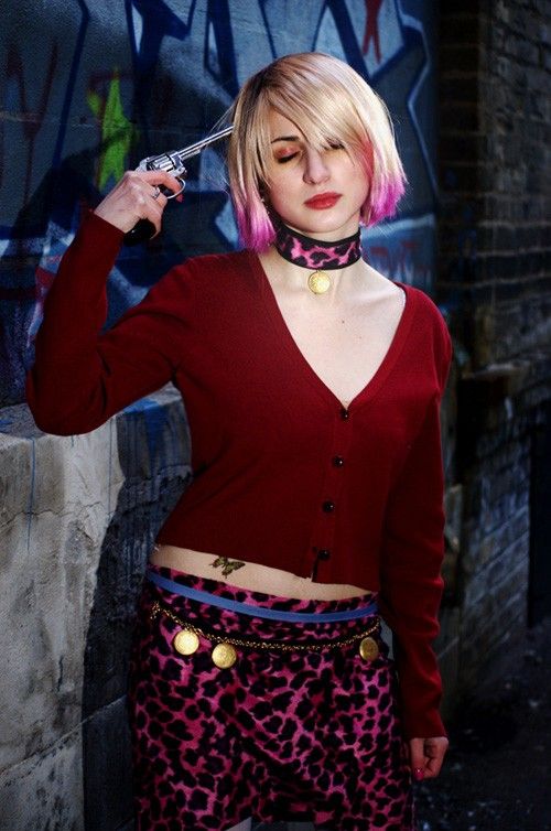 a woman with pink hair is standing in front of a graffiti covered wall and holding a knife