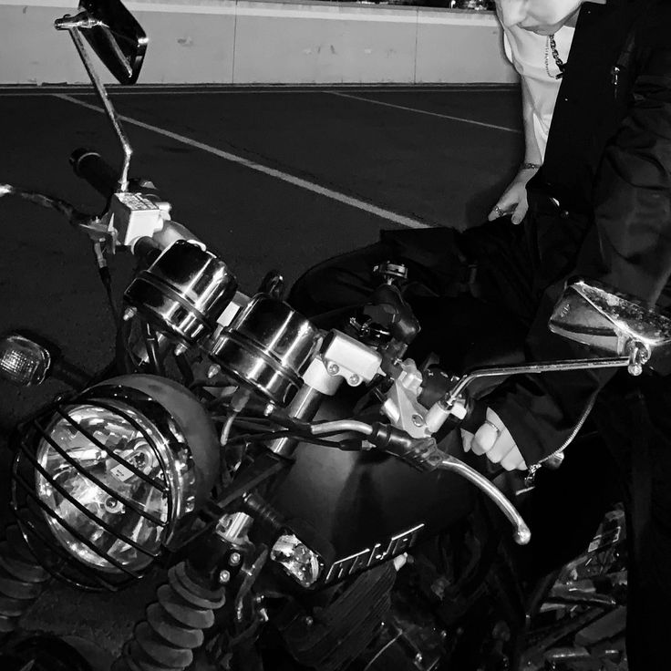 black and white photograph of a man leaning on a motorcycle with his hand on the handlebars