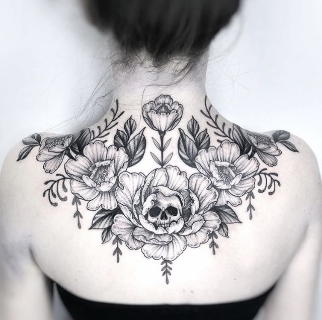 the back of a woman's neck with flowers and leaves tattooed on her chest