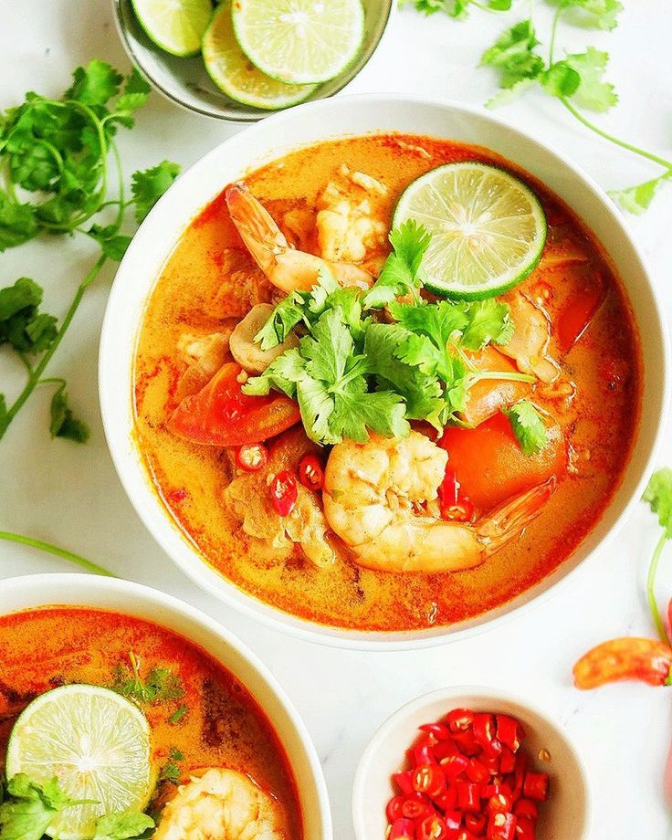 three bowls filled with soup and garnished with cilantro, limes, and shrimp