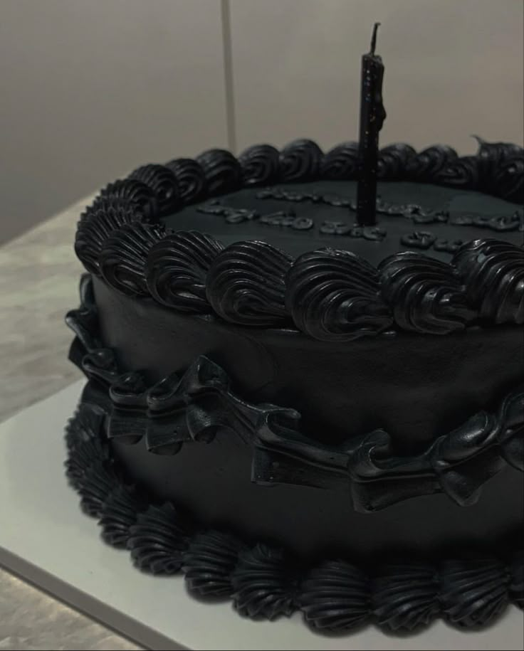 a black cake sitting on top of a white counter with a single candle sticking out of it