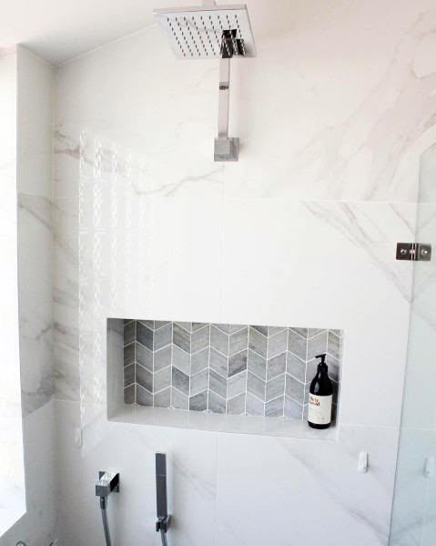 a bathroom with white marble walls and flooring, including a shower head mounted on the wall