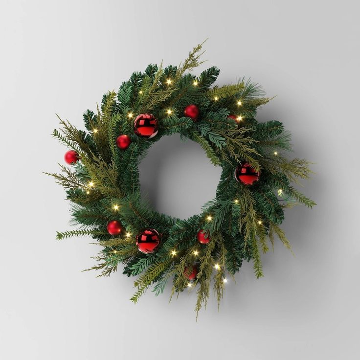 a christmas wreath with red and green ornaments hanging from the side on a white wall