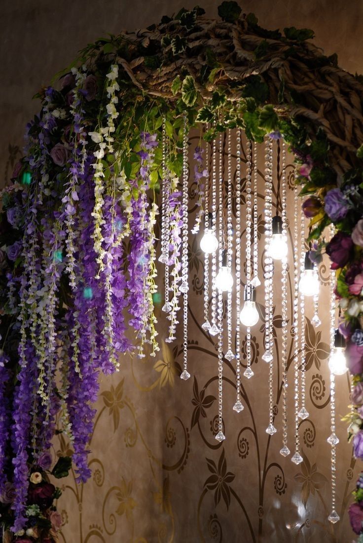 a chandelier with purple flowers hanging from it's sides and lights in the middle