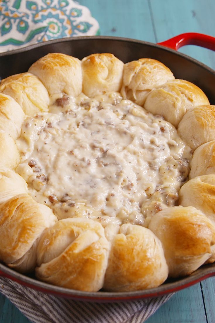 a pan filled with rolls covered in cream cheese sauce on top of a blue wooden table