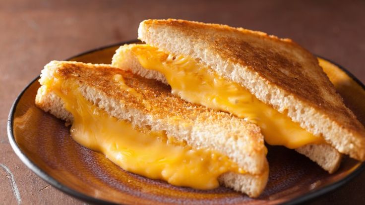 two grilled cheese sandwiches sitting on top of a wooden plate