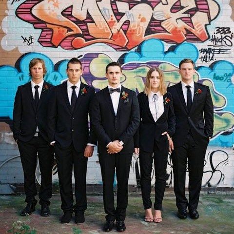 a group of young men standing next to each other in front of a graffiti covered wall