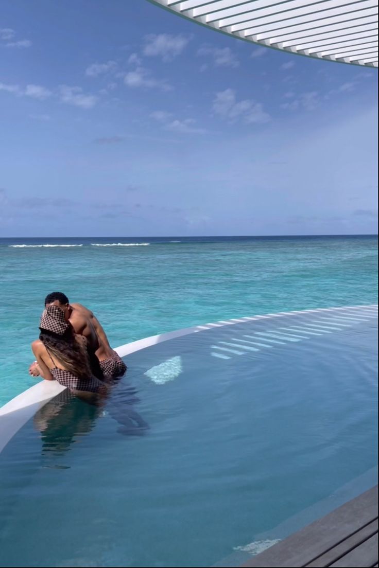 a man and woman sitting in the middle of a swimming pool next to each other