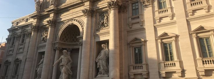 an ornate building with statues on the front and side walls, in sunlight from behind