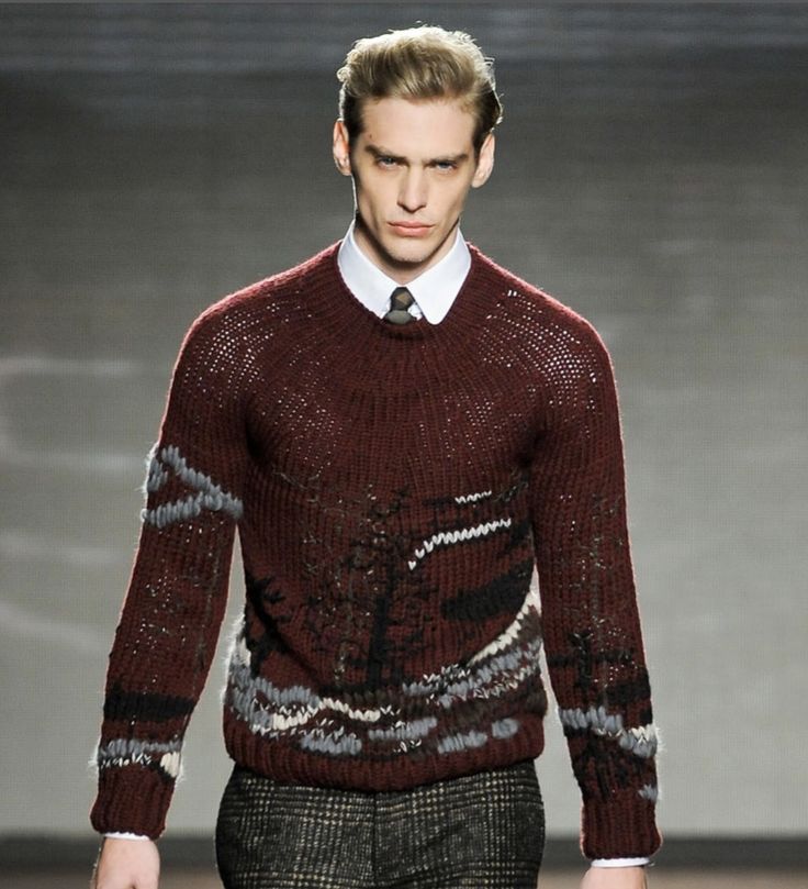 a man in a sweater and tie walks down the runway