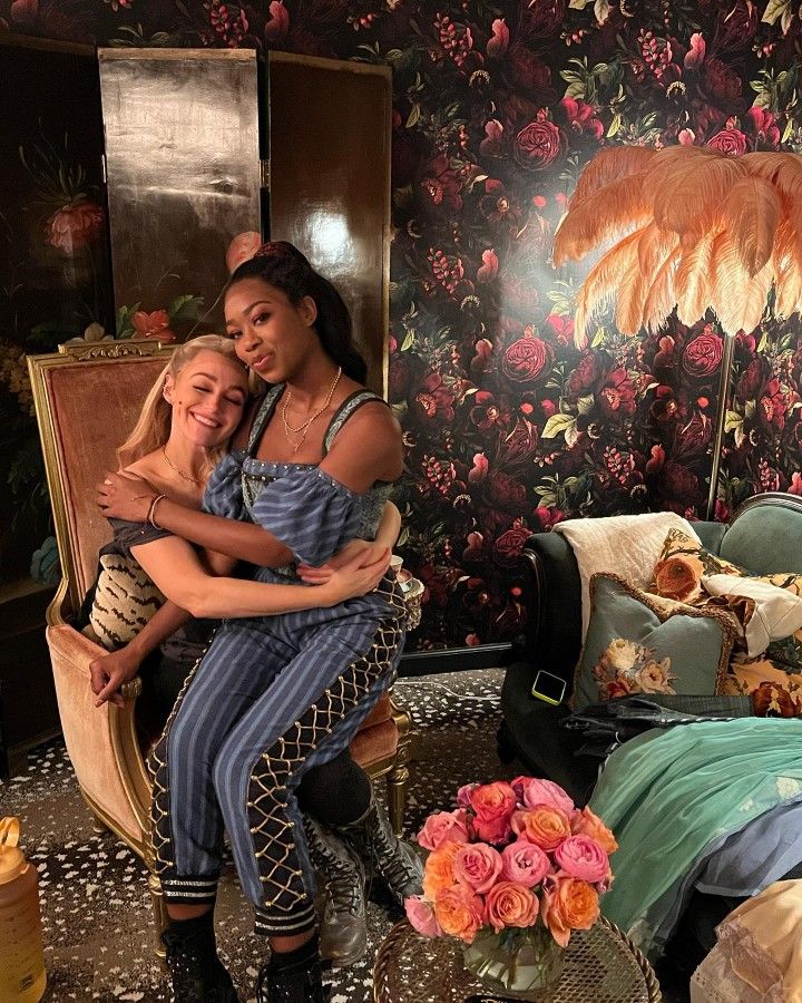 two women are hugging each other in a room with floral wallpapers and furniture