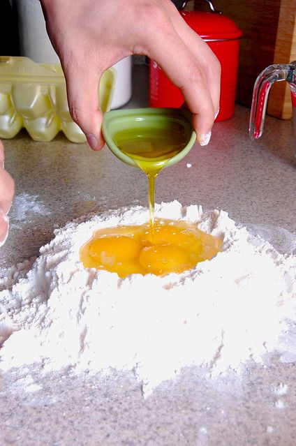 a person pouring something into a bowl on top of a table with flour and other ingredients