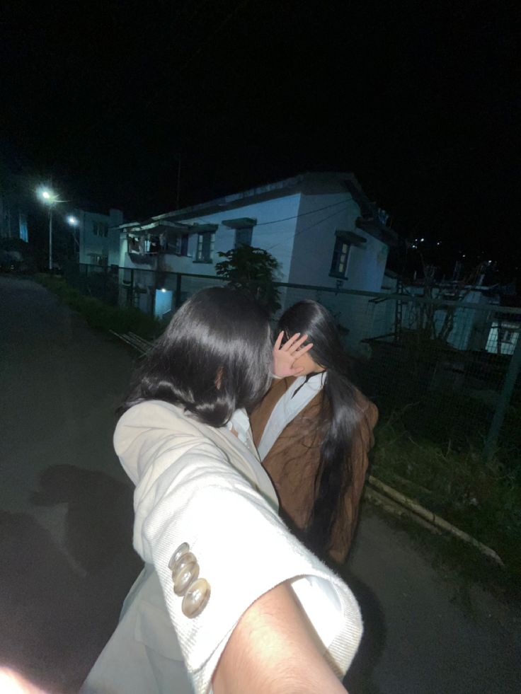 two people standing on the side of a road at night with their arms around each other