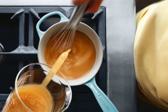 a person pouring liquid into two glasses in front of a stove top with other cooking utensils