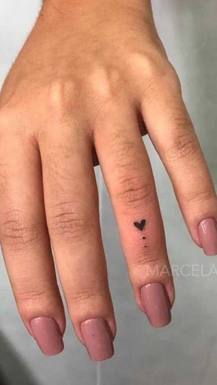 a woman's hand with a small black heart tattoo on her left thumb and finger