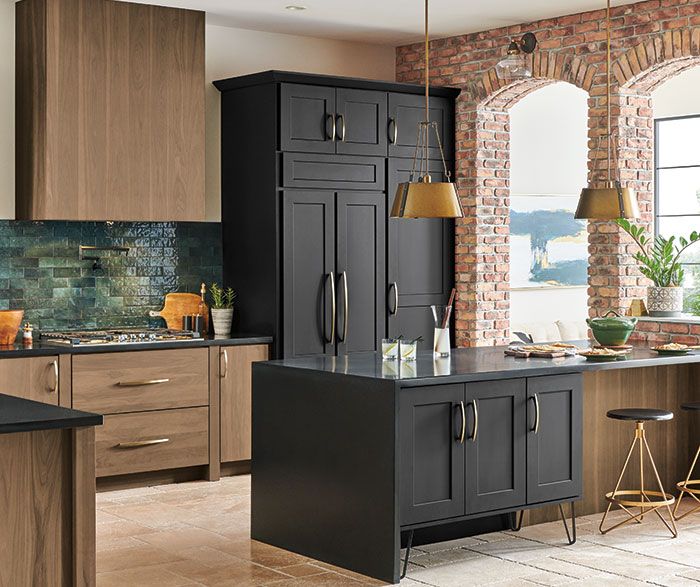 a kitchen with black and brown cabinets, an island countertop and stools in front of a brick wall