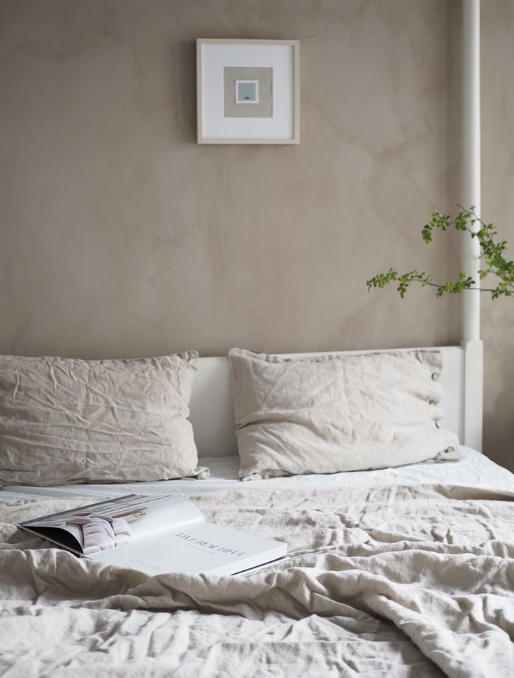 an unmade bed with white linens and a plant on the nightstand next to it