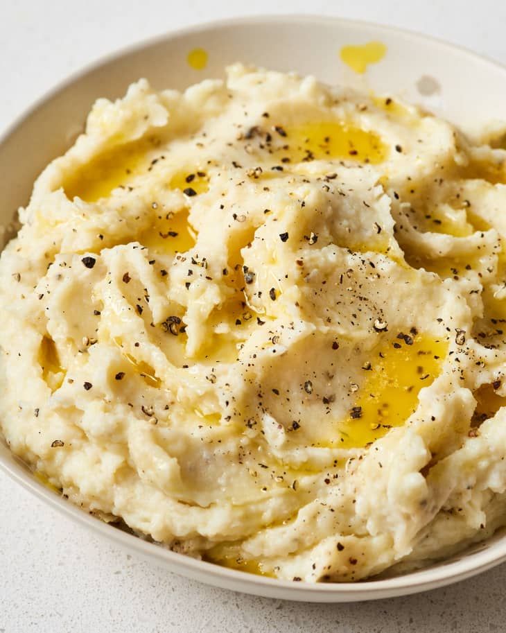 mashed potatoes in a white bowl topped with olive oil and seasoning sprinkled on top