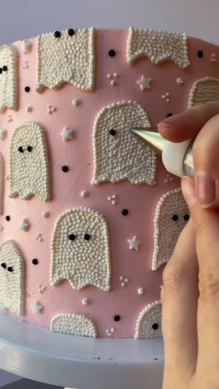 a woman is decorating a pink cake with white frosting