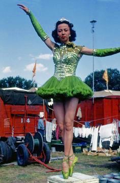 a woman in a green dress standing on top of a wooden block with her arms outstretched