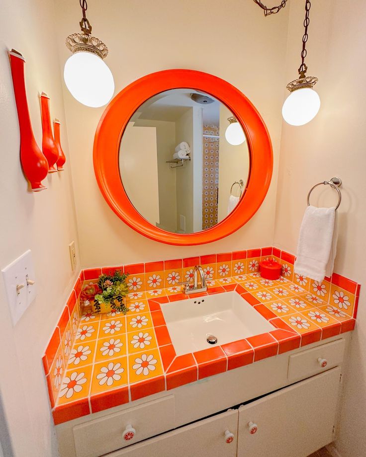 a bathroom with orange and white tile on the counter top, sink and mirror above it