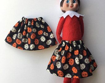 an elf doll is wearing a black and orange dress with pumpkins on it, next to a halloween themed skirt