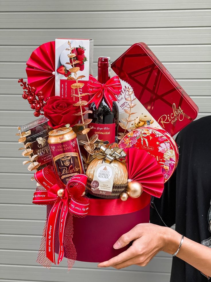 a woman holding a red gift box filled with wine and chocolates in front of a garage door