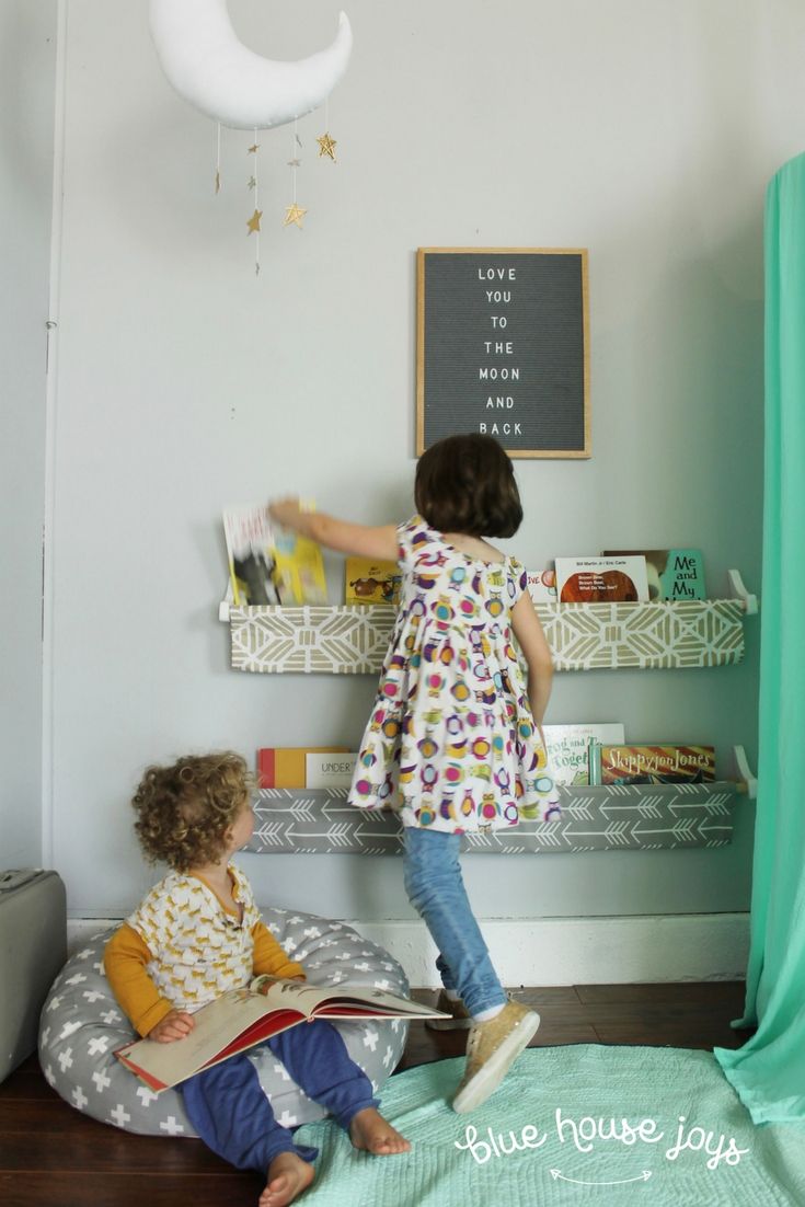 two young children are playing with books in their playroom, while the moon hangs above them