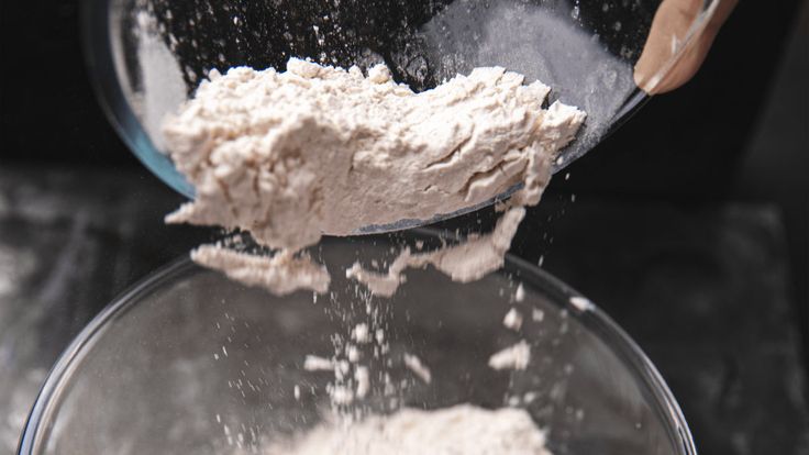 a person pouring flour into a glass bowl