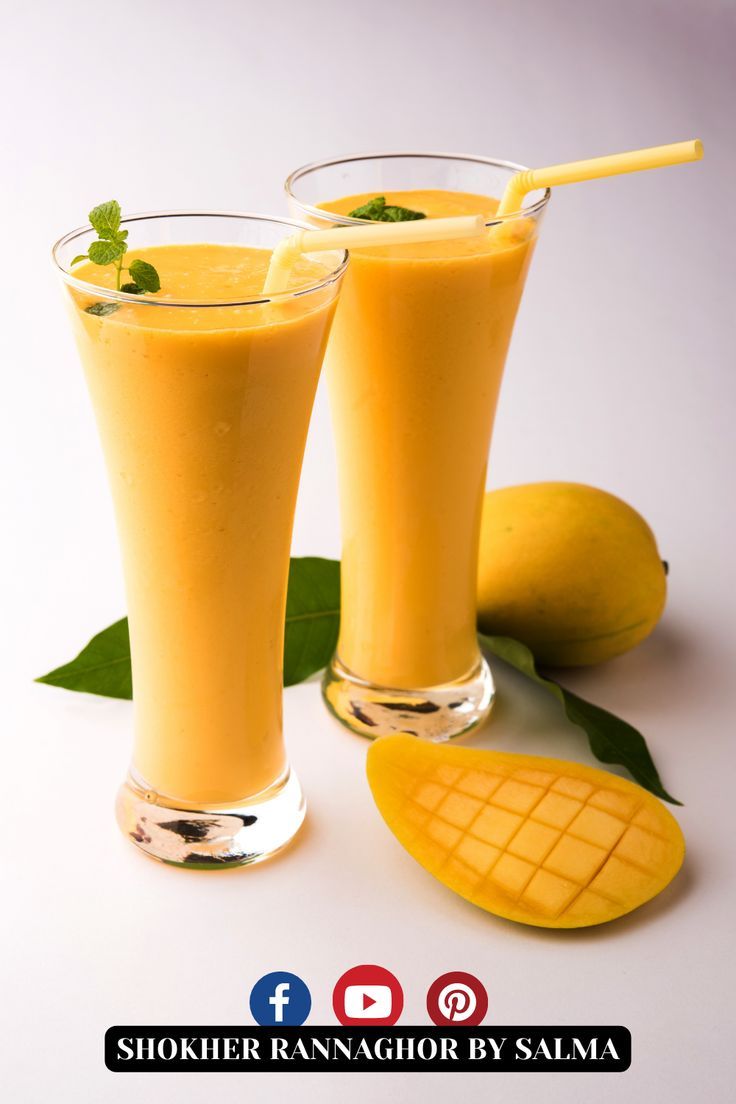 two glasses filled with orange juice and garnished with green leaves next to sliced mangoes