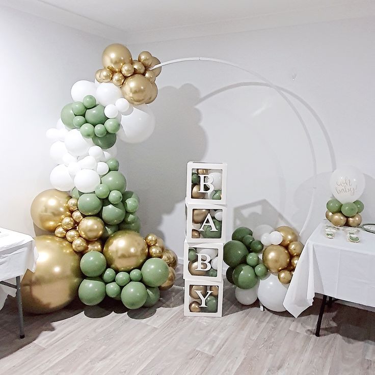 a room filled with balloons and decorations for a baby's first birthday party in gold, green and white