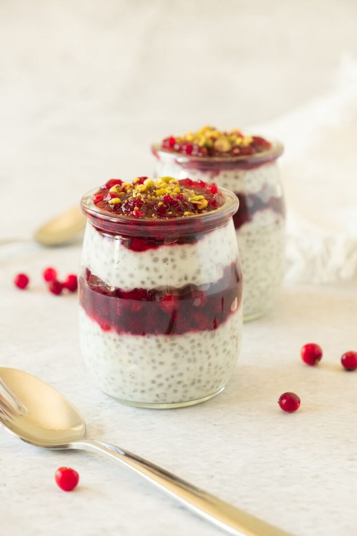 two jars filled with chia pudding and topped with cranberry sauce next to a spoon