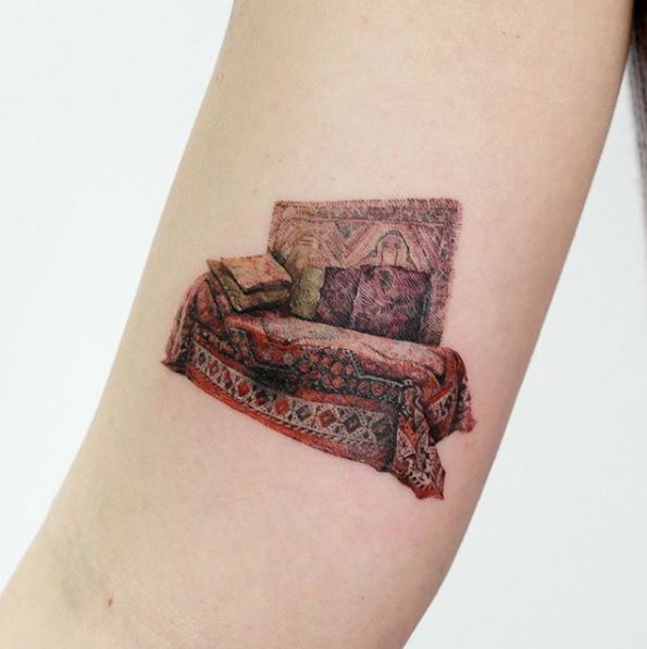 a woman's arm with a small tattoo of a couch and pillows on it