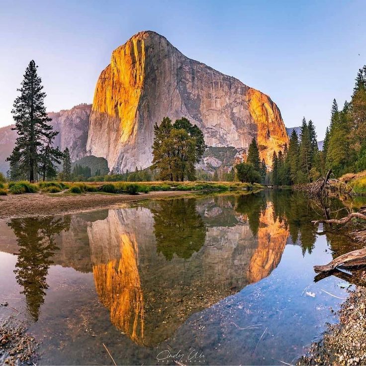 the mountain is reflected in the still water near the river's edge, with trees and rocks around it