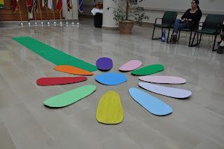 a group of people sitting on chairs in a room next to a flower made out of colored paper