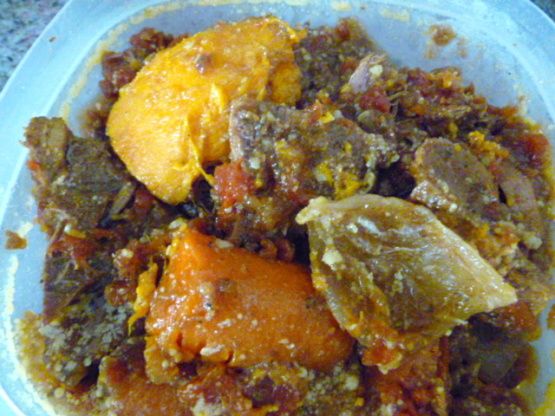 a bowl filled with meat and vegetables on top of a stone counter next to an orange slice